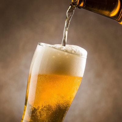 Image montrant un verre de bière en train d'être rempli depuis une bouteille. La bière, de couleur dorée, forme une mousse blanche abondante au sommet du verre. Des bulles sont visibles à travers le liquide, renforçant l'idée de fraîcheur. L'arrière-plan 