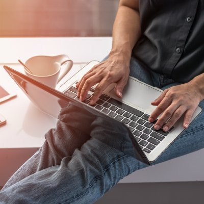 Photo montrant une personne avec les mains posées sur le clavier d'un ordinateur portable, posé sur ses jambes, en train de rédiger un article de blog dans une atmosphère décontractée.