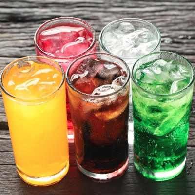Image montrant cinq verres remplis de boissons colorées avec des glaçons. Chaque verre contient un liquide de couleur différente : orange, rouge, brun, transparent et vert, représentant probablement des sodas ou des boissons rafraîchissantes variées. Les 