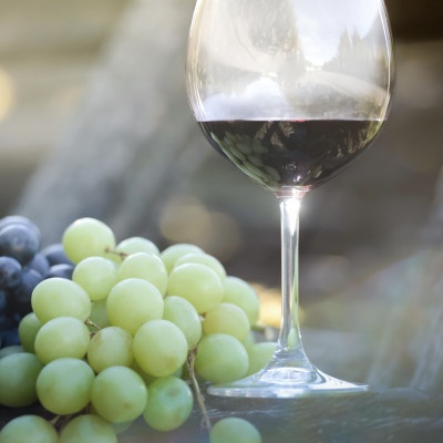 Image montrant un verre de vin rouge posé à côté d'une grappe de raisins verts. La lumière naturelle éclaire délicatement la scène, créant une ambiance apaisante et chaleureuse. En arrière-plan, les raisins et le verre de vin sont mis en valeur par un flo